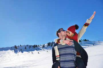 Young couple having fun on snow. Happy man at the mountain giving piggyback ride to his smiling...