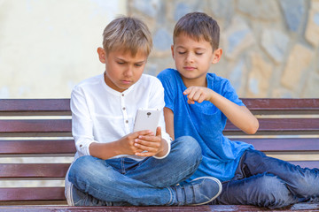 Boys with mobile phone sitting on the bench outdoors