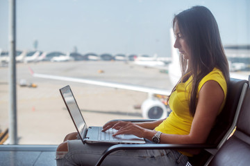 Young woman holding a laptop on lap typing keyboard indoors in airport