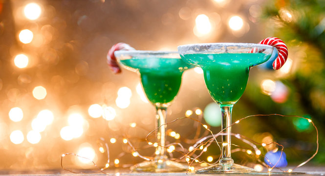 Christmas image of two wine glasses with green cocktail, caramel sticks