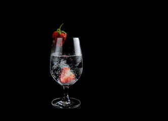 Sparkling water with strawberry in a high glass on black background.