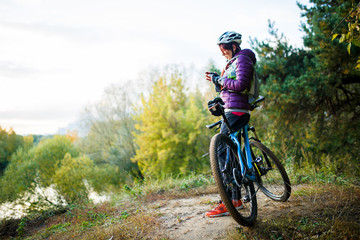 Photo of girl in helmet standing with phone in hands near bicycle