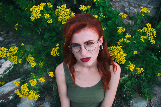 Mujer joven con gesto de tristeza posando junto a flores amarillas 