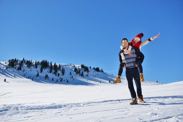 Young couple having fun on snow. Happy man at the mountain giving piggyback ride to his smiling...