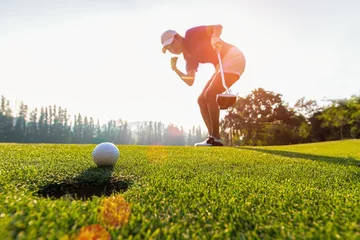 Rollo Asiatische Golfspielerin, die nach langem Golfball auf dem grünen Golf, Sonnenuntergang, Kopienraum gewinnt. Gesundes Konzept © freebird7977
