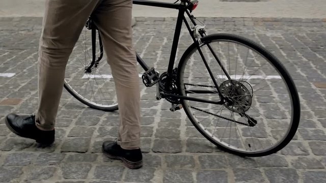 Slow motion footage of young man walking on street and getting on old vintage bicycle