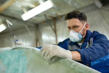 Portrait of mature man wearing protective mask repairing boat while working in yacht workshop,...