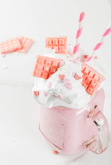 Crazy shake, romantic milkshake for Valentine's day with strawberry, white chocolate and sugar candy hearts, on white background, copy space