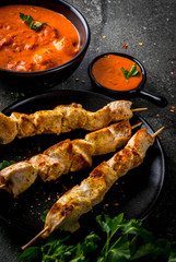 Indian food. Traditional dish spicy chicken tikka masala, butter chicken curry, with indian naan butter bread, spices, herbs. Served in bowl. sauce, on skewers. Stone dark table. copy space