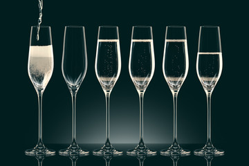pouring champagne into six transparent glasses on black