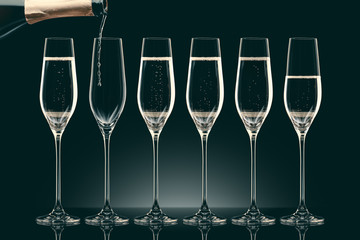 pouring champagne from bottle into six transparent glasses on black