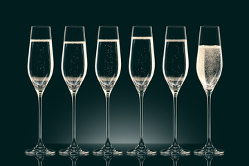 six transparent glasses with champagne on black