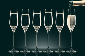 pouring champagne from bottle into six transparent glasses on black