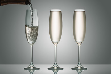 pouring champagne from bottle into three glasses on grey