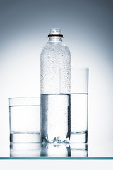 plastic bottle and glasses of clean water on reflective surface