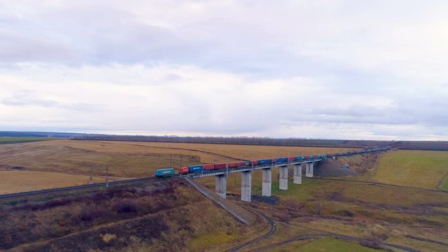 A long line of intermodal containers crosses a railway bridge.  