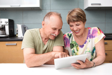 Happy senior couple using tablet in kitchen at home
