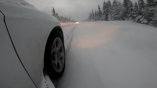 A car with a studded tires driving on a wintry road at dusk with oncoming cars