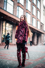 Outdoor portrait of young beautiful happy smiling girl posing on street. Model wearing stylish warm clothes. Magic snowfall. Christmas, new year, winter holidays concept.