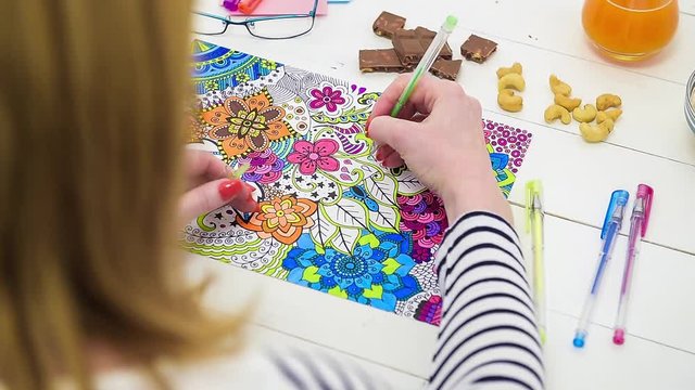 Color video of a young unrecognisable woman coloring an adult coloring book. Over the shoulder look. New stress relief trend.