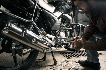 Young man in leather jacket fixing motorcycle in garage