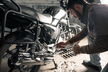 Fototapeta na wymiar Young man in leather jacket fixing motorcycle in garage