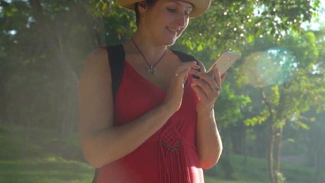 The smiling woman travels with a backpack around the island. girl using a phone texting on smartphone app on grasses in garden. The woman will erase the card at herself in the smartphone. Vietnam..