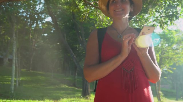 The smiling woman travels with a backpack around the island. Woman close up. girl using a phone texting on smartphone app on grasses in garden