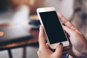Mockup image of woman's hands holding mobile phone with blank black desktop screen in cafe