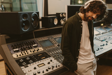 sound producer in headphones leaning back on recording equipment at studio