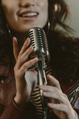 cropped shot of female singer performing song with vintage microphone