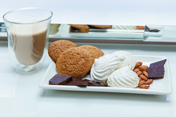A glass of coffee with biscuits, chunks of chocolate, marshmallows and nuts on a white table.A glass of coffee with Sweets