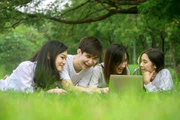 Asian group of friends talking and laughing with using laptop in green lawn in the park