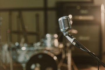 Close-up shot of vintage microphone on stand against blurred drum set - Powered by Adobe