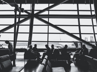 Passengers sit in airport terminal departure gate waiting area Silhouette people in modern building