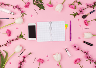 working, womanhood, fashion concept. in the frame crafted of beautiful flowers and equipment for make up there is iphone and small linned notebook with colorful stickers