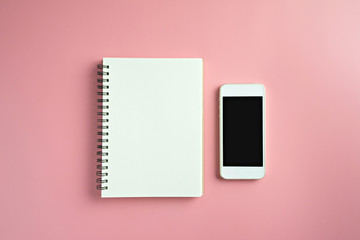 Top view of blank notebook and mobile phone on pink background.