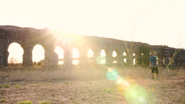 Young man in sportswear running along ancient roman aqueduct Appio Claudio. Training outdoor alone in peaceful park in Rome at sunset slow motion.