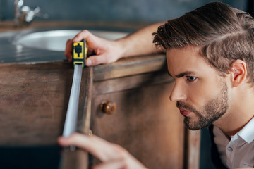 close-up view of young foreman measuring kitchen furniture with tape