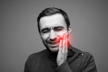Man with a toothache. Pain in the human body on gray. Black and white photo with red dot