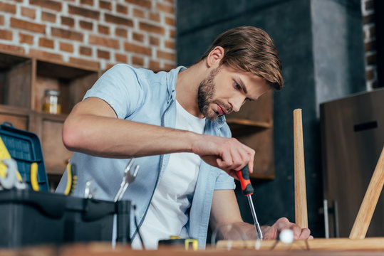 focused young man repairing stool with screwdriver