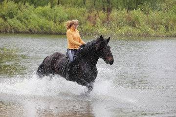 Blonde woman riding horseback in a shallow riverbed
