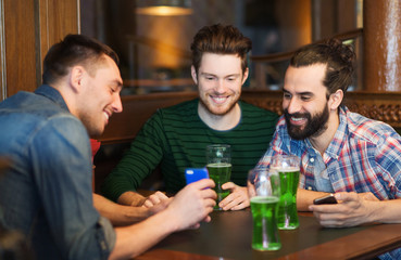 friends with smartphone drinking green beer at pub