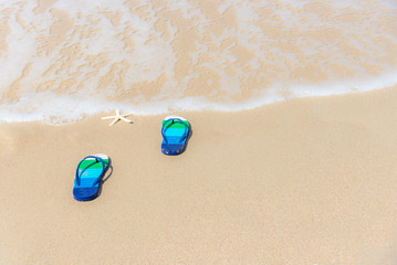 Fototapeta na wymiar Sandals on a splashing water sandy ocean beach, relax and freedom. Summer vacation concept.