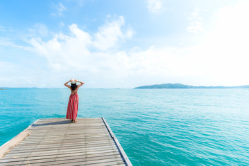 Summer Day. Smiling women relax and wearing red dress fashion standing on the wooden bridge over the sea, blue sky background. Travel and Vacation. Freedom Concept
