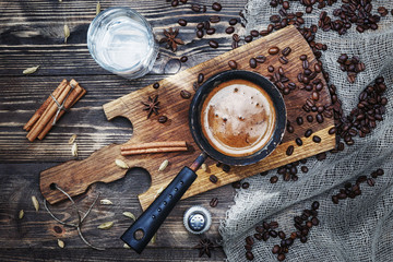 .coffee in cezve on a rustic wooden table with spices, cinnamon, water, salt and coffee beans near...