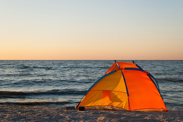 bright orange yellow tent empty, sunrise on the seashore, in the sun, against the blue sea and blue sky, yellow sand, beach, rest, summer