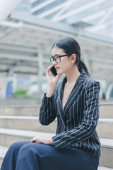 Fototapeta premium Asian businesswoman is using smartphone while sitting on stair outside office