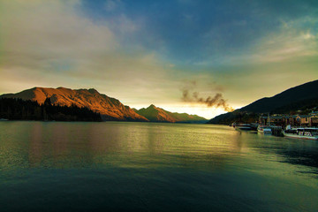 Awesome sunset view of southern Alps landscape with Lake Wakatipu, mountains of Cecil and Walter Peak with famous Queenstown steamship, New Zealand South Island, holiday resort city of Queenstown