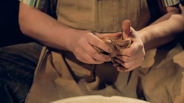 Strong potters hands knead a piece of clay. 